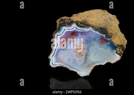 Polierter Schnitt aus natürlichem Achat-Edelstein mit roher brauner Oberfläche auf schwarzem Hintergrund. Schöner glatter, eisblauer Querschnitt von Chalcedonmineralien. Stockfoto