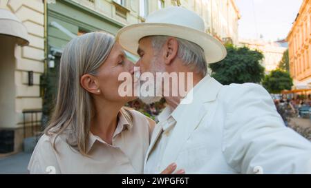 Glückliche ältere kaukasische Touristen Paar Senior Mann Frau nimmt Selfie Streaming Video romantisch Küssen Handy moderne Technologien außerhalb der Stadt Stockfoto