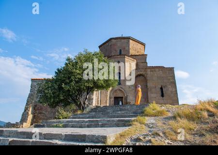 Ein Mädchen in einem orangefarbenen Kleid und einem weißen Schal steht neben der alten Kirche Stockfoto