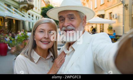 Porträt fröhlich lächelndes kaukasisches Paar ältere Erwachsene glückliche Familie Mann Ehemann Frau Frau posiert vor Straßencafé und fotografiert Selfie Stockfoto