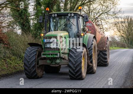 John Deere 6630 Traktor zieht einen Tröpfelstreuer auf einer Landstraße in Irland. Stockfoto