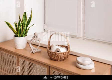 Korb mit Toilettenpapierrollen, Zimmerpflanzen und Holzschrank im Badezimmer Stockfoto