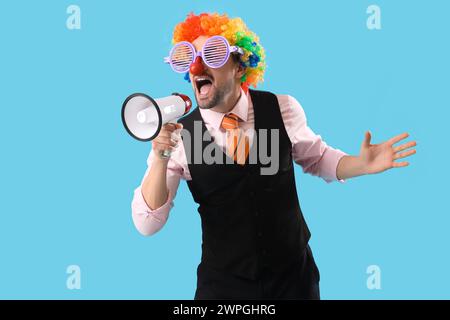 Junger Geschäftsmann in lustiger Verkleidung mit Megaphon, der auf blauem Hintergrund schreit Stockfoto
