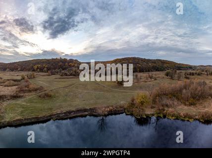 Luftflug über dem Fluss im Herbsttal mit Schilf und Feldweg. Fluss Siwerskyi Donets in der Ukraine ländliche Landschaft Stockfoto