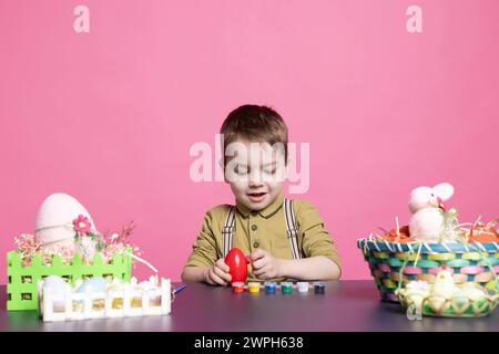 Entzückender kleiner Junge, der schöne Arrangements für Ostersonntag macht und Eier mit Stempeln und Pinseln bemalt. Das entzückende Kind verwendet gerne Bastelmaterialien, um im Studio zu dekorieren. Stockfoto