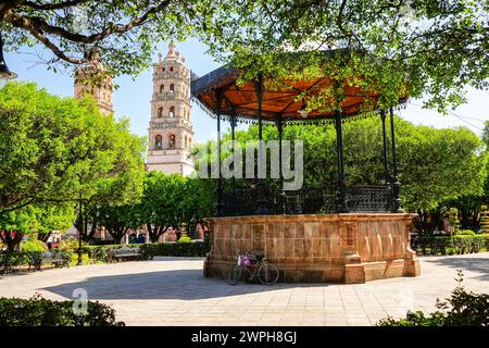 Die Zwillingsglockentürme der Pfarrkirche Nuestra Señora de la Luz oder die Kirche unserer Lieben Frau vom Licht, und die Bühne im Jardin de Salvatierra Park im zentralen historischen Viertel von Salvatierra, Guanajuato, Mexiko. Die neogotische Kirche aus dem 17. Jahrhundert ehrt die Patronin der Stadt. Stockfoto