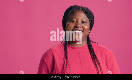 Video mit stylischer afroamerikanischer Frau mit Vorliebe für pinkfarbene Pullover-Mode und selbstbewussten, auffälligen Posen. Echtes Lachen der jungen Dame verleiht der Nahaufnahme authentischen Charme. Stockfoto