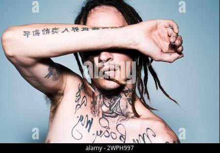 Junger Hipster. Mode tätowierten Kerl mit Dreadlocks Dreadlocks auf grau. Stockfoto