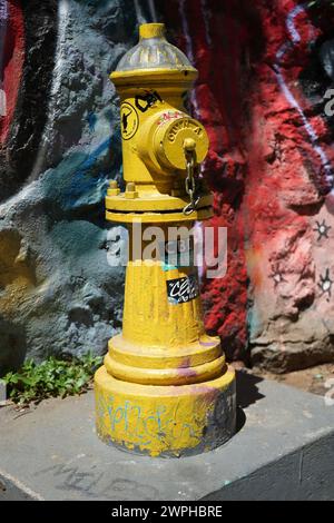 Rustikaler gelber Hydrant mit blauem und rotem Hintergrund in der Sonne Stockfoto