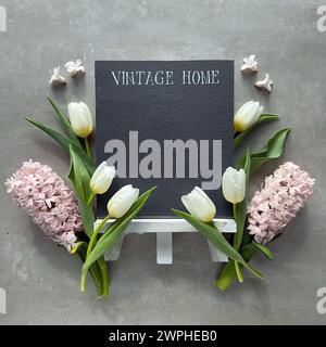 Eine leere Tafel mit den Worten Vintage Home und Kopierraum umgeben von Frühlingsblumen Stockfoto