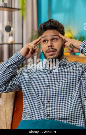 Kranker, kranker indischer Mann, der Schläfen reibt, um Kopfschmerzen zu heilen, leidet unter Spannung und Migräne, Stress, grimmige Schmerzen, Bluthochdruck zu Hause. Der Hindu-Typ drinnen auf der Couch. Vertikal Stockfoto