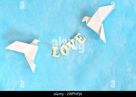 Verbreite Botschaft des Liebeskonzepts. Zwei weiße Tauben Origami mit Wort LIEBE auf blauem Hintergrund. Stockfoto