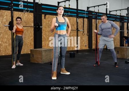 Junge Mädchen, die mit anderen Athleten mit Widerstandsband, starkem Bizeps oder Bauchmuskeln im Fitnessstudio trainieren Stockfoto