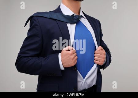 Geschäftsmann trägt Superheldenkostüm unter Anzug auf beigefarbenem Hintergrund, Nahaufnahme Stockfoto