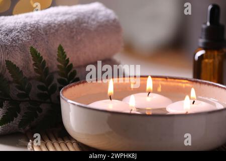 Spa-Zusammensetzung. Brennende Kerzen in der Schüssel, Handtücher und eine Flasche ätherisches Öl auf dem Tisch, Nahaufnahme Stockfoto