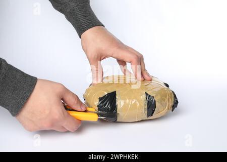 Schmuggel und Drogenhandel. Mann, der ein Paket mit Betäubungsmitteln mit einem Koffer auf weißem Hintergrund öffnet, Großaufnahme Stockfoto