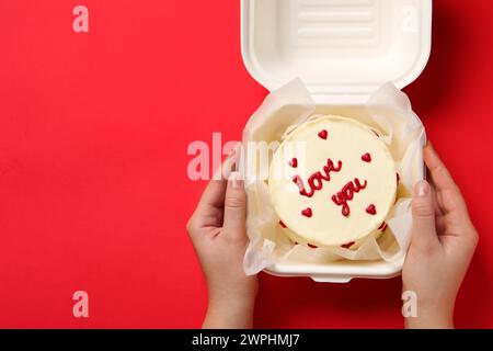 Frau, die eine Kiste mit bento-Kuchen am roten Tisch hält, Nahaufnahme. St. Valentinstag-Überraschung Stockfoto