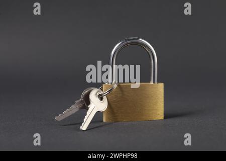 Vorhängeschloss aus Stahl mit Schlüsseln auf dunkelgrauem Hintergrund, Nahaufnahme Stockfoto