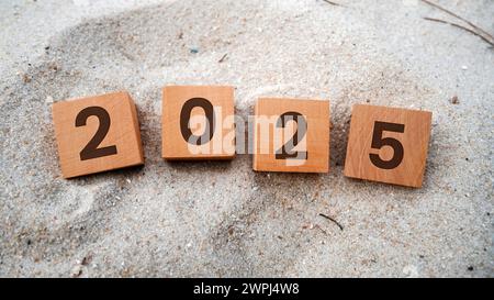 2025 auf Holzschnitt. Frohe Weihnachten und frohes neues Jahr, Sandhintergrund. Ideenkonzept für das neue Jahr 2025. Stockfoto