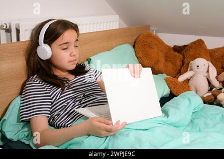 Der Computer im Bett ist müde und das Mädchen schläft ein. Im Bett mit Computer Stockfoto