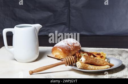 Gerollte Pfannkuchen mit Hüttenkäse und Rosinen und ein Teil Hüttenkäse-Auflauf auf Teller. Hausgemachtes Brötchen mit Marmelade mit Puderzucker und Milch j Stockfoto