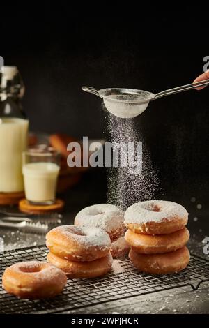 Süße Donuts mit Puderzucker und ein Glas Milch, fotografiert auf schwarzem Hintergrund Stockfoto