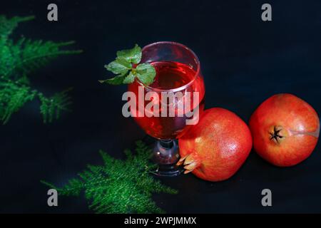 Top View Engel von reifem Granatapfel und Glas Wein auf schwarzem Hintergrund und mehr Blumen im besagten. Stockfoto