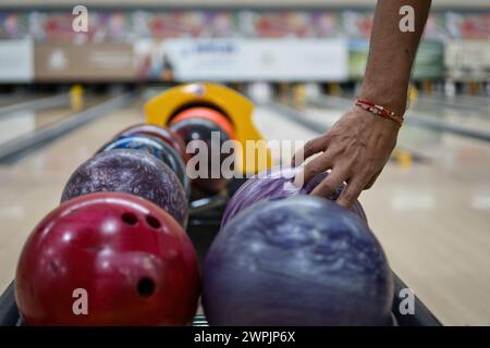 Handaufnahme von Bowlingbällen in der Rückgabemaschine auf der Bowlingbahn. Spuren und Pins in unscharfem Hintergrund. Stockfoto
