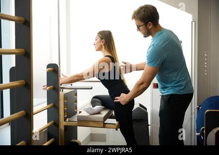 Der Ausbilder im Gesundheitszentrum hilft der Frau, an einem speziellen Simulator zu arbeiten Stockfoto