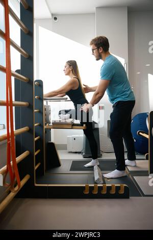 Mitarbeiter der Rehabilitationsklinik hilft Frau bei der Arbeit an einem speziellen Simulator Stockfoto