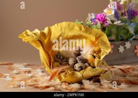 Krepppapiernester mit ostereiern, Federn und Frühlingsblumen auf beigefarbenem Hintergrund. Konzentrieren Sie sich auf einen Vordergrund. Stockfoto