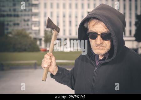 Aggressiver älterer Mann mit Axt unter dem Einfluss von Drogen im Park Stockfoto