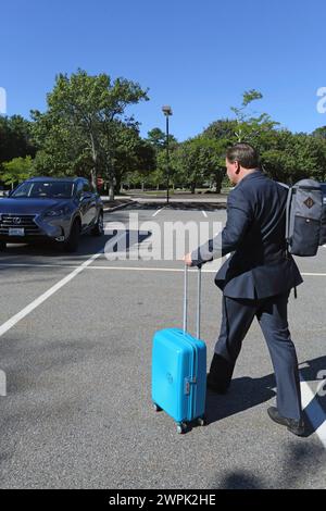 Seitenansicht eines männlichen Geschäftsreisenden, der seinen Koffer zum Auto rollte. Stockfoto
