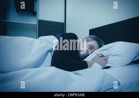 Der Polizist wacht in seinem Schlafzimmer auf und hat Angst vor Eindringlingen Stockfoto