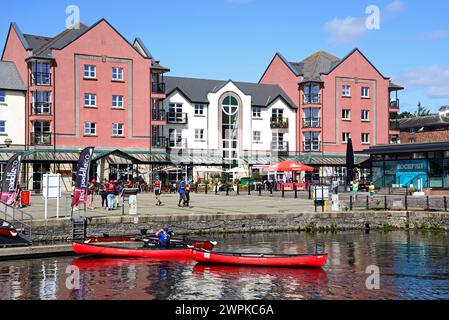 Menschen fahren Kajakfahren auf dem Exeter Schiffskanal mit Cafés und Restaurants auf der Piazza Terracina auf der Rückseite, Exeter, Devon, Europa. Stockfoto