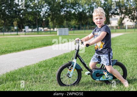 Ein kleiner Junge, der im Sommer mit Helm auf seinem Fahrrad fährt Stockfoto