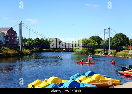 Kanufahrer auf dem Fluss exe mit der Cricklepit-Hängebrücke nach hinten und Tretbooten im Vordergrund, Exeter, Devon, Großbritannien, Europa. Stockfoto