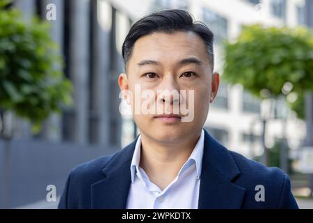 Ein professionelles Porträt eines asiatischen Geschäftsmannes in einem Anzug, das Vertrauen und Entschlossenheit vermittelt, im Freien aufgenommen. Stockfoto