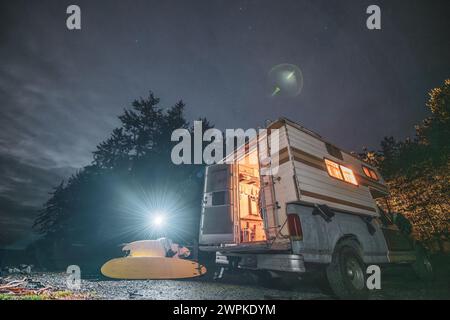 Frau, die auf einem Picknicktisch neben dem Wohnmobil sitzt, während der Surftour Stockfoto