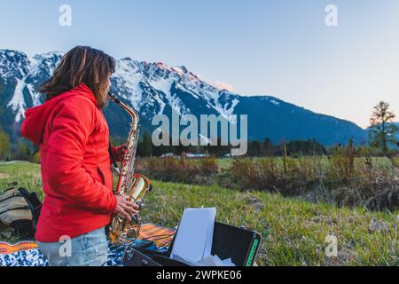 Frau spielt Saxophon bei Sonnenuntergang vor verschneiten Bergen Stockfoto