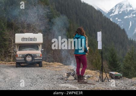 Frau spielt Saxophon in den Bergen neben dem Wohnmobil Stockfoto