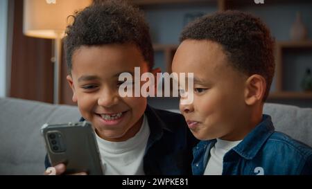 Zwei afroamerikanische kleine Jungen Brüder lachen beim Surfen auf dem Handy ohne Eltern schlechtes Verhalten, Kinder der jungen Generation und moderne Technologie Stockfoto