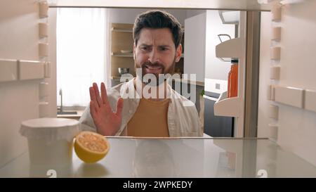 POV-Blickwinkel vom Inneren des Kühlschranks hungriger kaukasischer Mann in der Küche öffnet leeren Kühlschrank mit der Hälfte Zitronen- und Marmelade-Joghurtglas nichts zu essen Stockfoto
