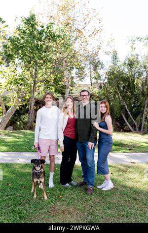 Vierköpfige Familie lächelt mit Hund im Park in San Diego nach Kamera Stockfoto