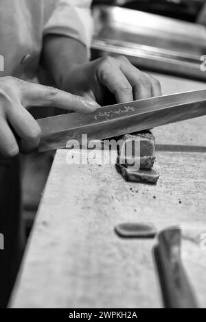 Nahaufnahme des Sushi-Chefkochs, der gebratenen Thunfisch mit einem Messer auf dem Schneidebrett schneidet. Stockfoto