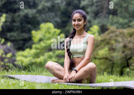 Die junge indische Frau im Trainingsanzug genießt eine ruhige Yoga-Session in einem grünen Park, die Frieden und einen gesunden Lebensstil verkörpert. Stockfoto
