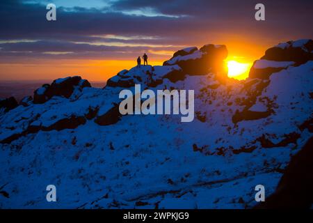 02/15 ohne Ende der Eiszeit, die das Land packt, stehen zwei Bergsteiger auf Felsen, um einen beeindruckenden Sonnenuntergang zu bestaunen Stockfoto