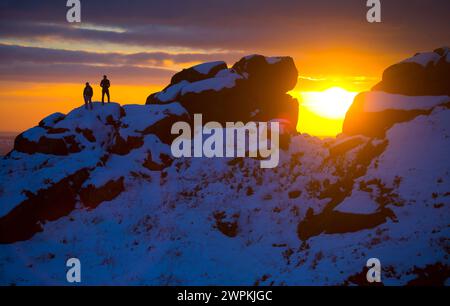 02/15 ohne Ende der Eiszeit, die das Land packt, stehen zwei Bergsteiger auf Felsen, um einen beeindruckenden Sonnenuntergang zu bestaunen Stockfoto