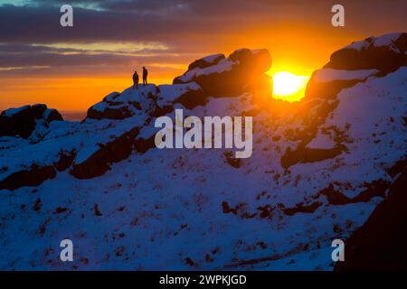 02/15 ohne Ende der Eiszeit, die das Land packt, stehen zwei Bergsteiger auf Felsen, um einen beeindruckenden Sonnenuntergang zu bestaunen Stockfoto