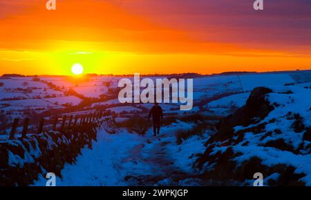 02/15 da kein Ende in Sicht ist wegen der kalten Bedingungen des Landes, hält ein Wanderer an, um einen beeindruckenden Sonnenuntergang über der Roache zu bestaunen Stockfoto